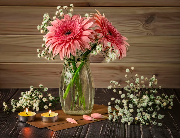 ガラスの花瓶にピンクのガーベラのロマンチックな花束カスミソウの花とキャンドルを装飾として