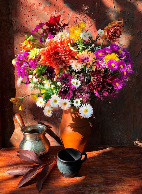 Romantic bouquet with flowers of dahlia chrysanthemum perennial aster montbrecia geyhera and grape leaf with cezve and coffee cup in sunlight on an old rusty background