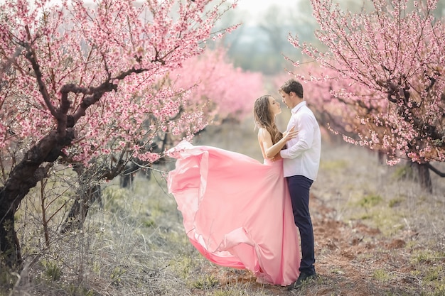 Romantic bridegroom kissing bride on forehead while standing against wall covered with pink flowers