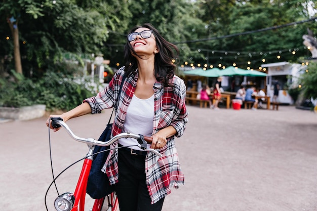 주말에 쉬면서 미소를 지으며 올려다보는 로맨틱한 브루네트 소녀, 자전거를 타고 웃고 있는 백인 여성의 야외 초상화
