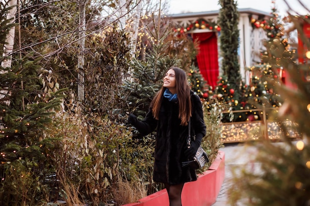 Romantic caucasian woman is choosing a fir tree at christmas fair outdoors beautiful woman is travel...