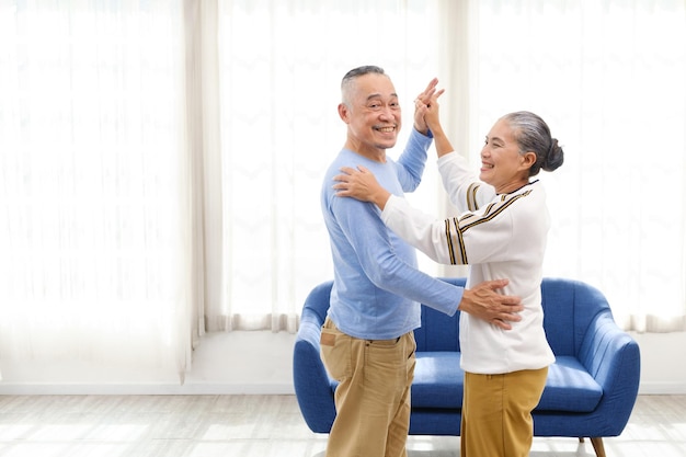 Romantic and cheerful Asian wellbeing senior couple enjoy dancing and holding hands to music together with smiles and happiness in the living room Senior retirement activity at home