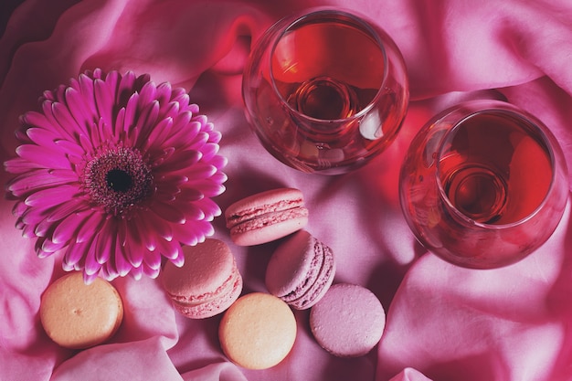 Romantic composition of flowers, sweets and wine on a pink background