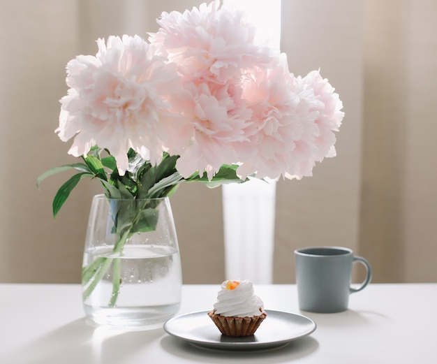 Romantic composition with beautiful pink peonies in a vase and a cup of coffee at home interior