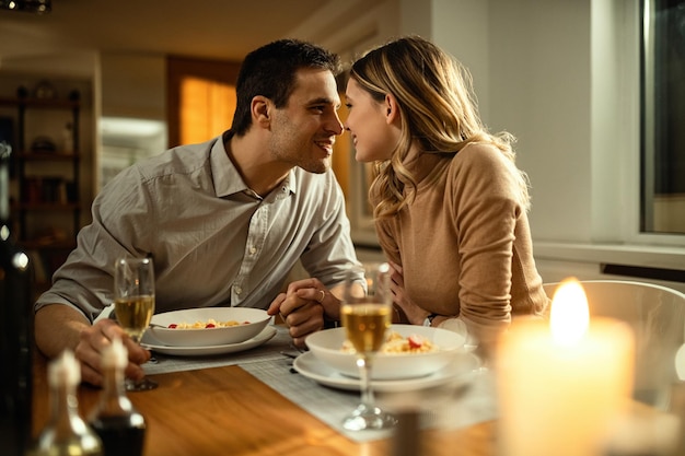 Coppia romantica in procinto di baciarsi mentre si tengono per mano durante la cena al tavolo da pranzo