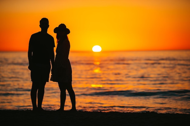 Romantic couple on the beach at colorful sunset on background