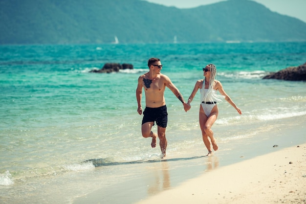 A romantic couple on the beach in a swimsuit, beautiful sexy young people. girl with  white dreadlocks and a man with a tattoo, having fun on the beach. Phuket. Thailand.