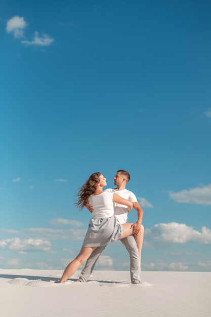 Dancing romantico delle coppie nel deserto della sabbia al fondo del cielo blu