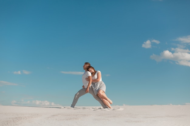 Dancing romantico delle coppie nel deserto della sabbia a cielo blu