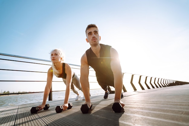 Romantic couple doing sport together at beach pier Two sporty athletes doing warmingup excersises