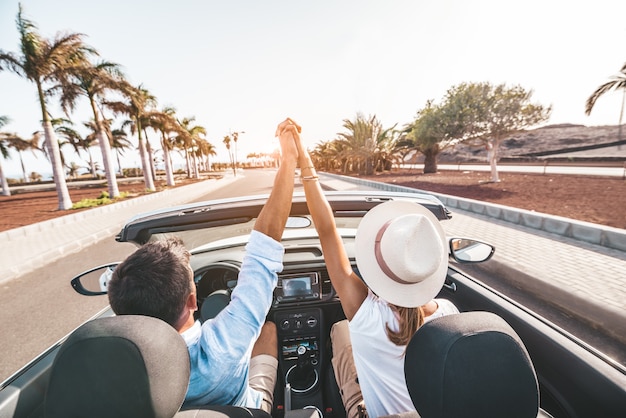 Romantic couple enjoying holidays driving a convertible car on the road at sunset.