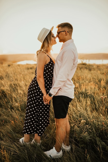 Romantic couple in a hat hug and kiss in the tall grass in the meadow.