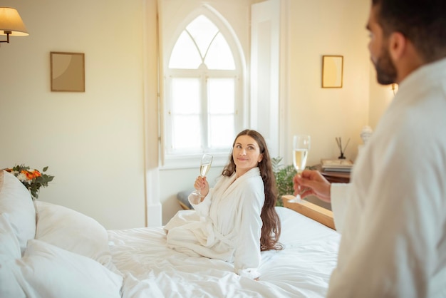 Romantic couple holding champagne glasses wearing comfortable bathrobes in hotel