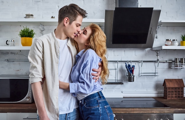 Romantic couple in the home kitchen. Beautiful woman and attractive man have a good time standing in the kitchen hugging and kiss