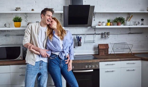 家庭の台所でロマンチックなカップル。美しい女性と魅力的な男性は、キッチンに立って抱き締めて楽しい時間を過ごします