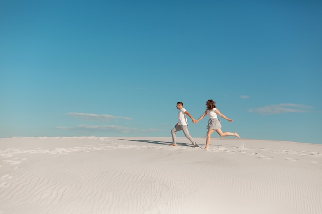 砂漠の白い砂の上を走る愛のロマンチックなカップル。