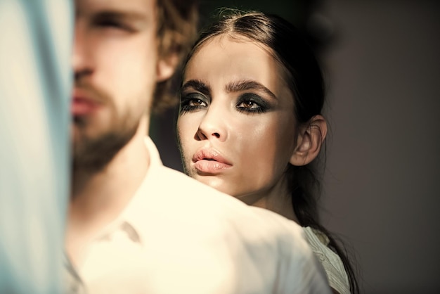 Romantic couple lying on bed Girl with makeup face Woman look out behind man shoulder Man with beard in shirt Cosmetics beauty visage concept Couple of fashion models