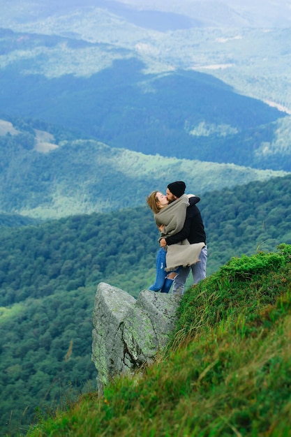 Romantic couple of pretty girl and handsome man in love kiss on cliff on summer day over mountain tops