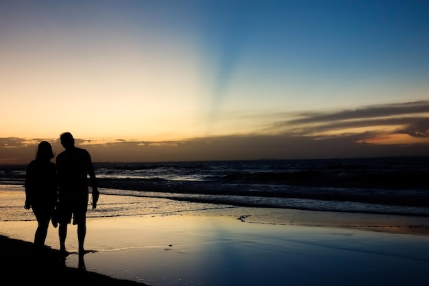 Romantic couple silhouette on sunset with colors reflecting in the sky and the sea