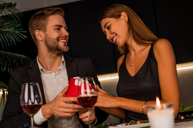 Romantic couple sitting at home kitchen and man giving gift box his female during romantic dinner