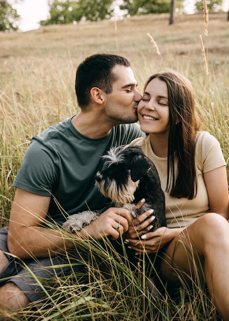 Photo romantic couple sitting outdoor hugging a miniature schnauzer dog smiling man kissing woman on cheek