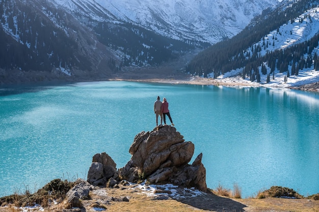 山の湖の見晴らしの良い場所にある岩の上に立つロマンチックなカップル
