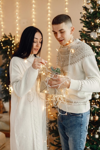 Romantic couple standing near Christmas tree and holding a gift box