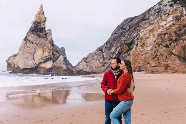 Photo a romantic couple stands on the coast hugging looks at the ocean