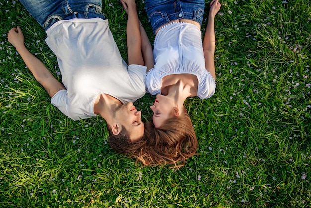 Romantic couple of young people lying on grass in park.