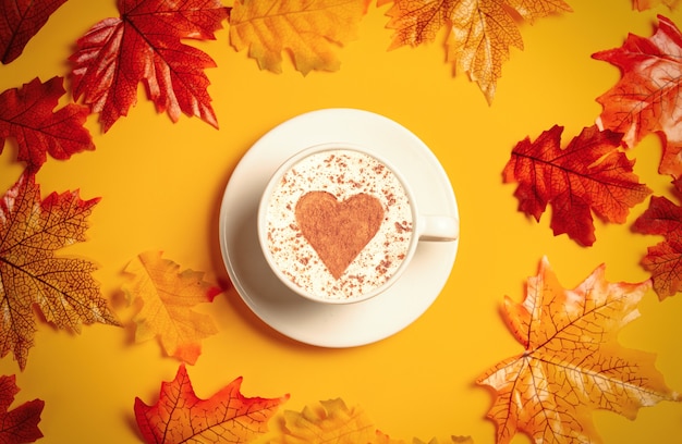 Romantic cup of coffee with autumn leaves on yellow background. Top view