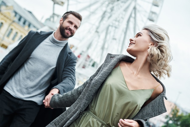 Romantic date outdoors young couple running at entertainment park holding hands looking at each