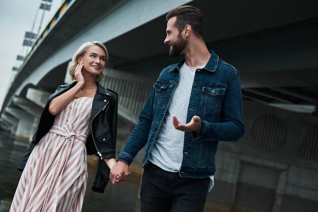 Romantic date outdoors young couple walking on the city street holding hands talking smiling joyful