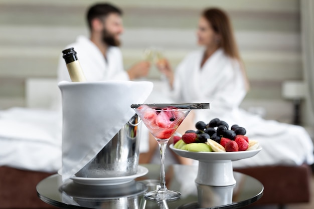 Романтический ужин в отеле из ягод и фруктов для молодой пары, пьющей шампанское в постели.