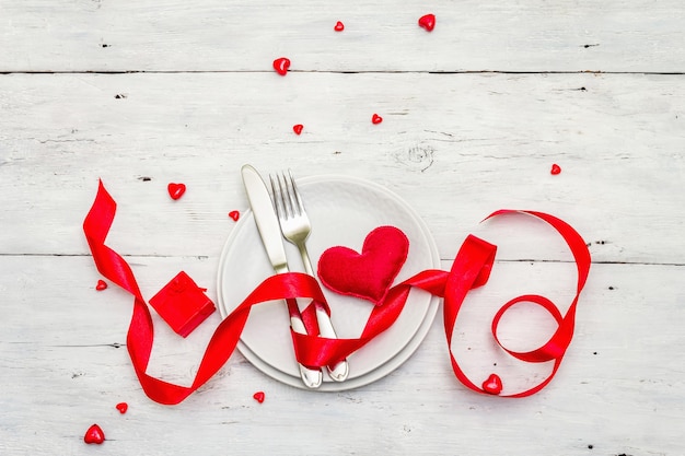 Tavolo da pranzo romantico. concetto di amore per san valentino o la festa della mamma, posate di nozze. morbido cuore in feltro, sfondo bianco di tavole di legno d'epoca