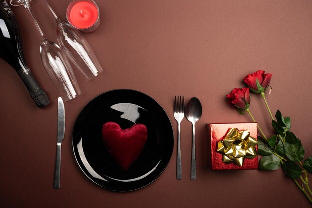 Photo romantic dinner table with red roses brown dark background candle red gift box and glasses