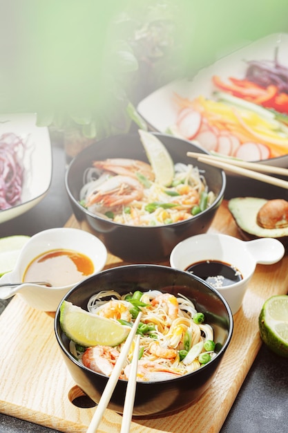 Romantic dinner for two asian cuisine rice noodles with shrimp\
and seafood green peas and onions soy sauce and various fresh\
vegetables romantic dinner in black plates with japanese\
chopsticks