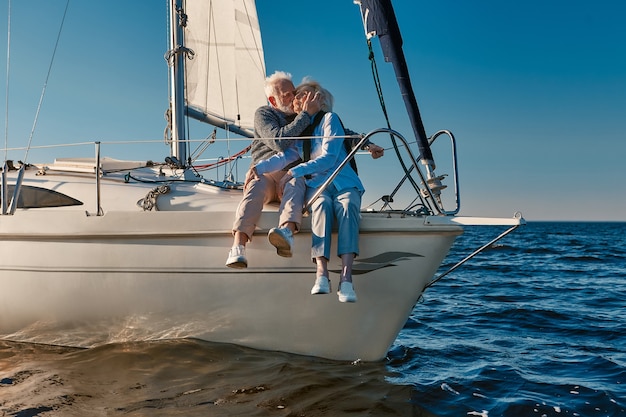 Romantic elderly couple embracing and kissing while relaxing on sail boat or yacht deck floating in