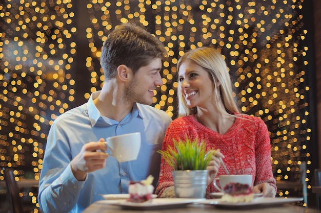 レストランでのロマンチックな夜のデート ワイングラスの紅茶とケーキを持つ幸せな若いカップル