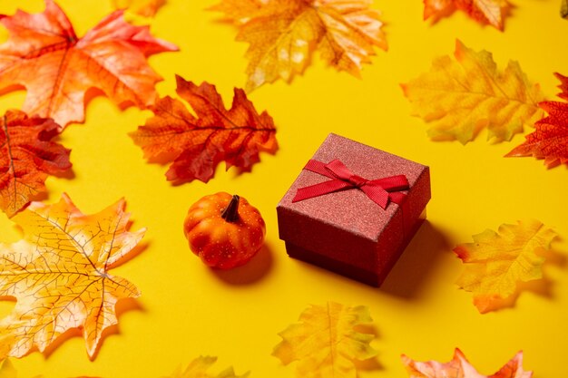 Romantic gift box with autumn leaves on yellow background. Top view