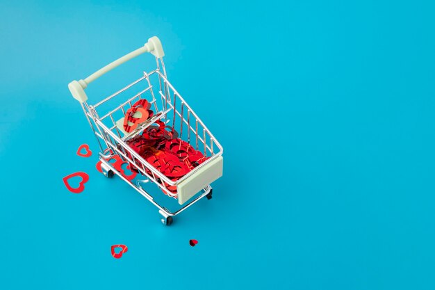 バレンタインデー、コピースペースのある青い背景のスーパーマーケットからのバスケットカートにたくさんのハートのロマンチックなギフトプレゼント