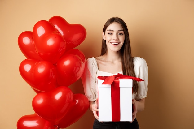 Romantic girl standing near heart balloons and holding surprise gift on Valentines day