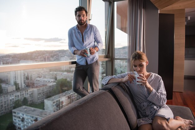 romantic happy young couple enjoying evening coffee and beautiful sunset landscape of the city while standing by the window