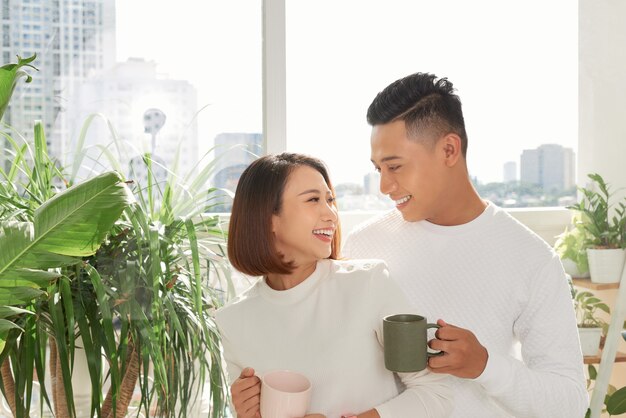 Romantic happy young couple enjoying morning coffee by the window on bright day at home