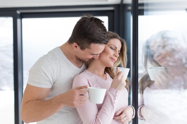 romantic happy young couple enjoying morning coffee by the window on cold winter day at home