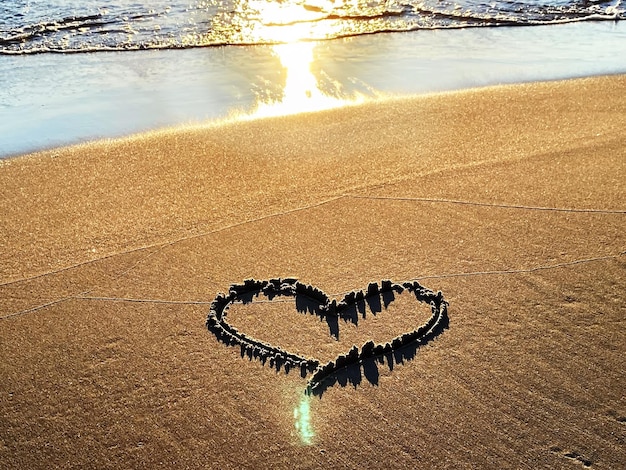 romantic heart symbol on beach sand at gold sunset sea water reflection