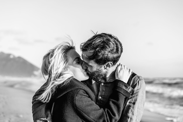 Romantic hipster couple in love kissing on shoreline at the wild beach