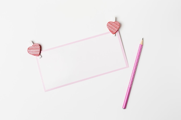 ロマンチックな手紙、ピンクの鉛筆と白い背景の上のハート型の装飾が施された白い空白のグリーティングカード、バレンタインデーおめでとうございます