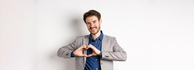 Romantic man in suit showing heart sign and smiling love his girlfriend standing on white background