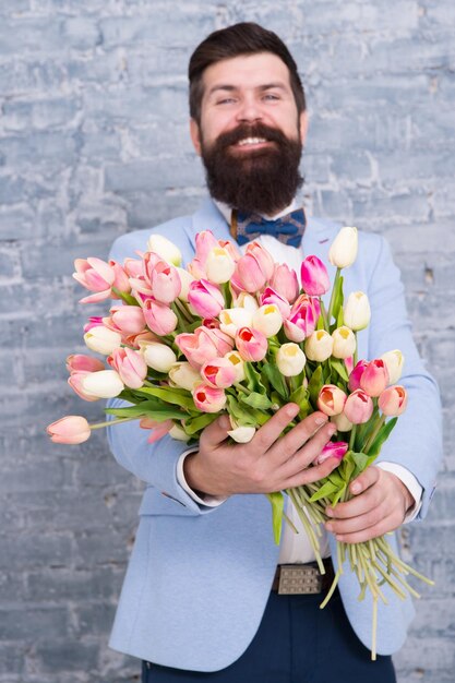 Romantic man with flowers Romantic gift Macho getting ready romantic date Tulips for sweetheart Man well groomed wear blue tuxedo bow tie hold flowers bouquet Waiting for his girlfriend