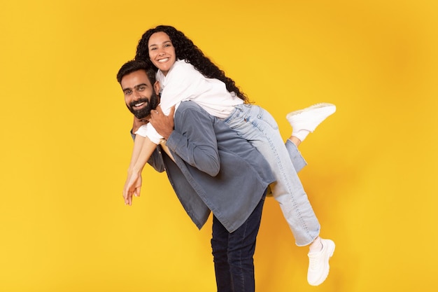 Romantic middle eastern man piggybacking his wife over yellow background